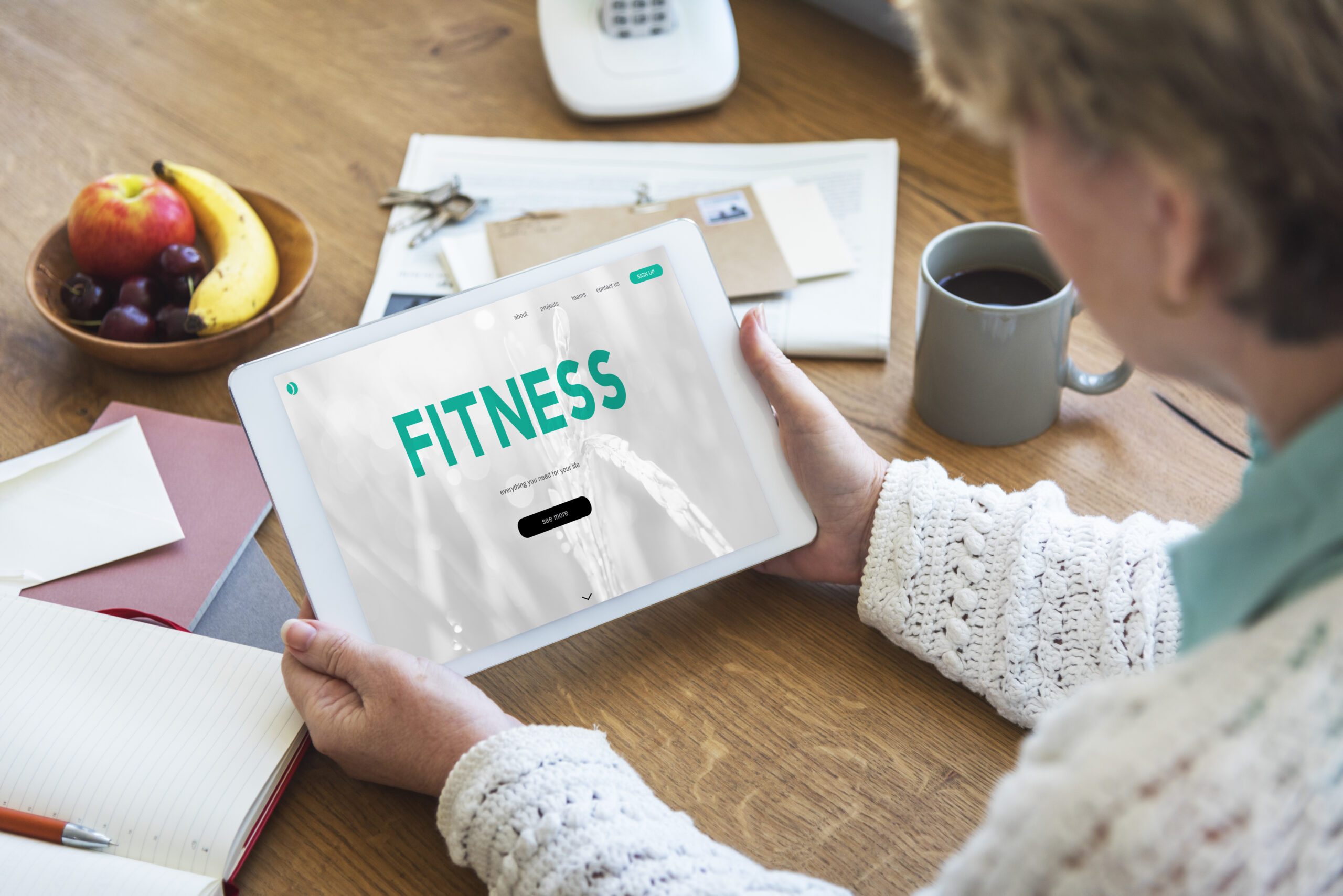 A woman writing fitness blog content ideas in a notebook with a laptop on the table.