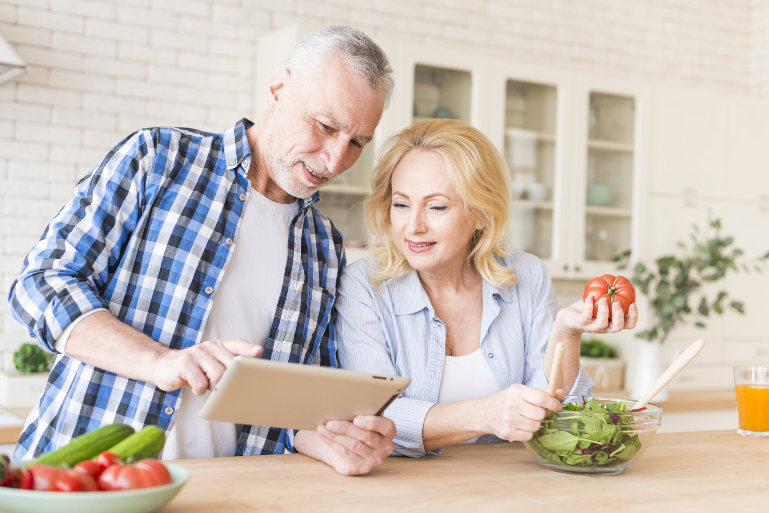 Senior couple preparing a heart-healthy meal while looking at a recipe on a tablet in a bright kitchen.