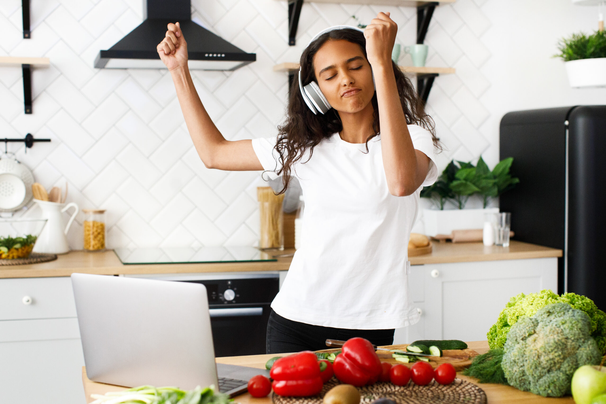 "Young African woman dancing in the kitchen while listening to music on headphones, staying active with 8 tips for working out when you’re just not in the mood."